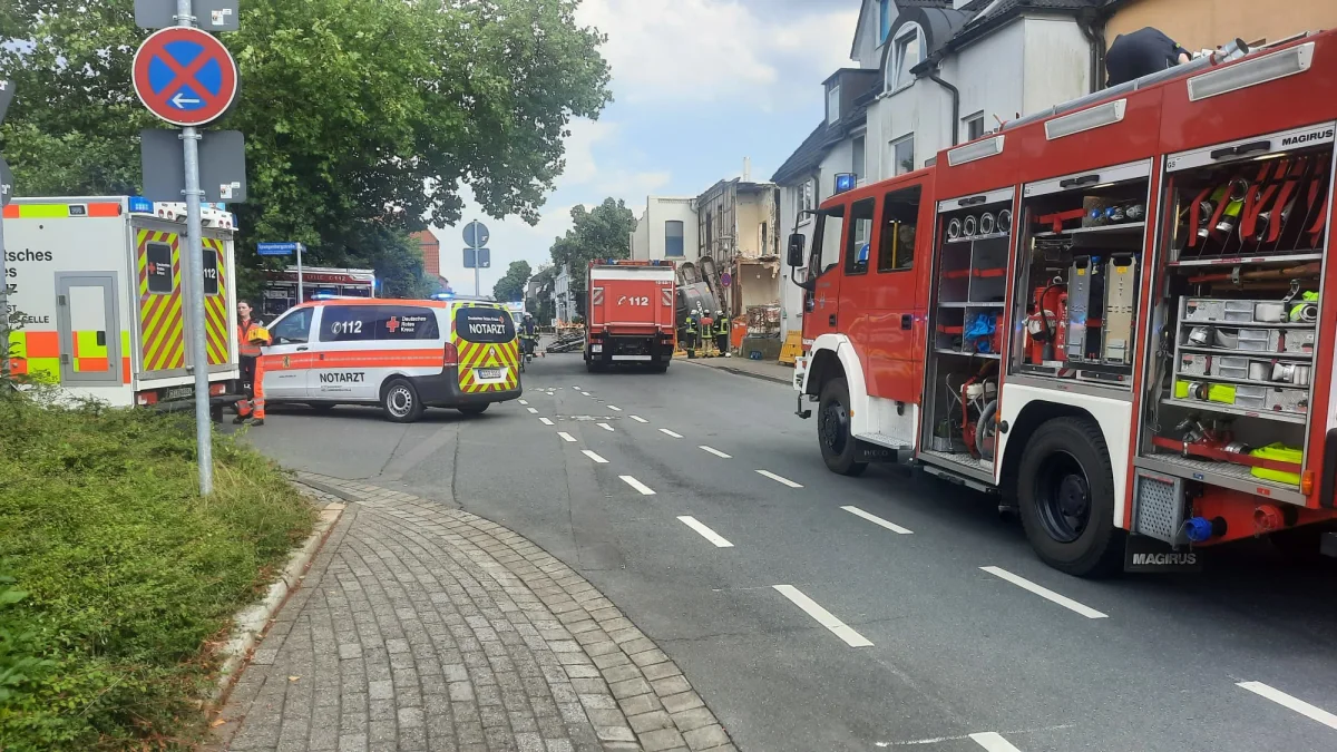 Einsatzfahrzeuge der Feuerwehr und des Notarztes stehen auf einer Straße vor einem Gebäude mit erheblichen Schäden an der Fassade.