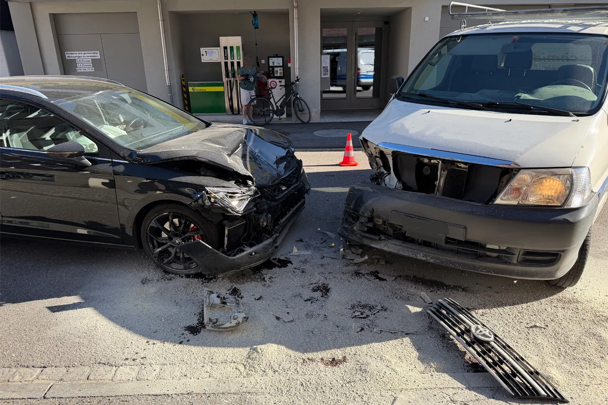 Ein schwarzes Auto und ein weißer Transporter mit erheblichen Frontschäden stehen vor einer Tankstelle nach einem Zusammenstoß.