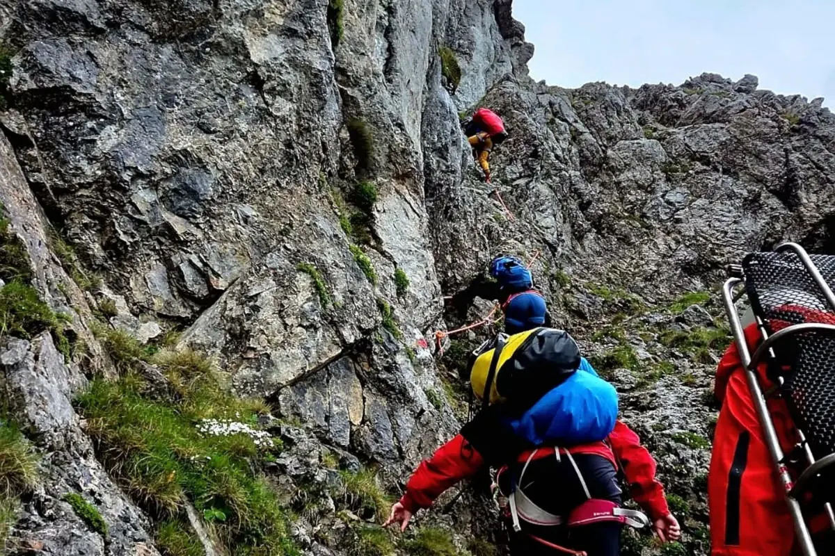 Eine Gruppe von Rettungskräften klettert über eine steile Felswand. Sie tragen Ausrüstung und sind angeseilt.