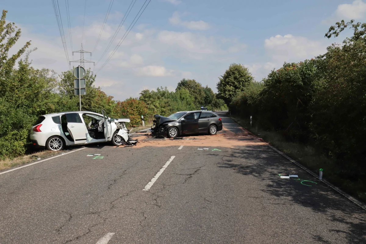 Auf einer ländlichen Straße sind zwei Autos frontal kollidiert. Beide Fahrzeuge sind stark beschädigt und stehen verkeilt auf der Fahrbahn.