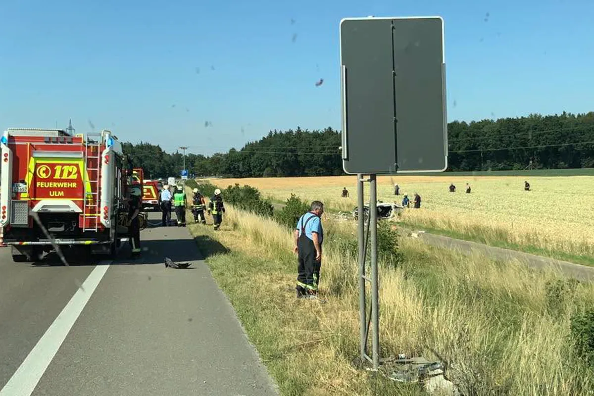 Ein Feuerwehrfahrzeug mit der Aufschrift 'Feuerwehr Ulm' steht auf einer Landstraße, mehrere Einsatzkräfte arbeiten am Straßenrand.