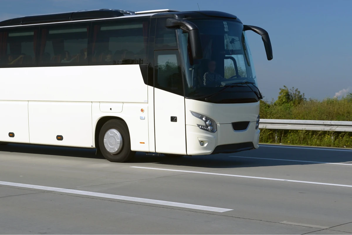Der weiße Reisebus fährt auf einer mehrspurigen Autobahn mit klaren Wetterbedingungen und wenig Verkehr.