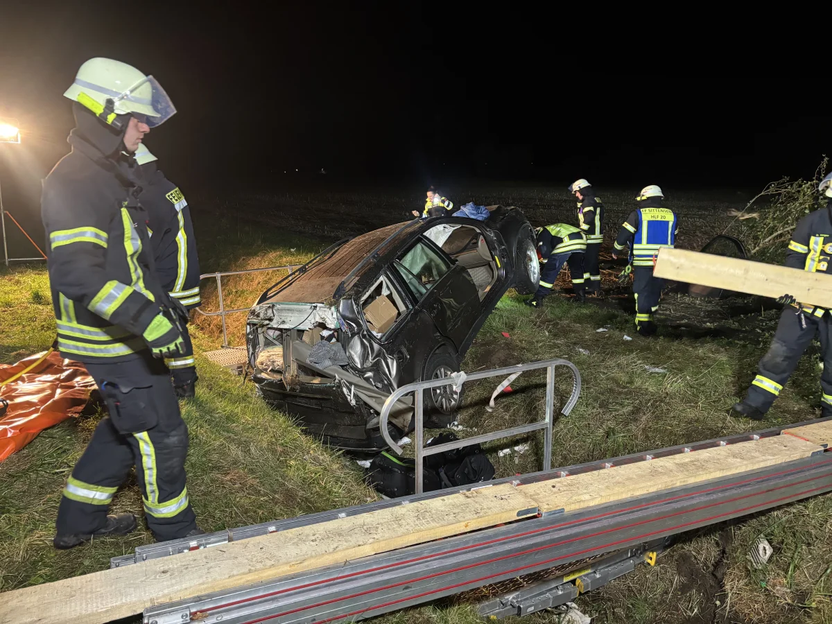 Mehrere Feuerwehrleute arbeiten an einem verunfallten Auto, das auf der Seite in einem Graben liegt. Sie sind bei Nacht im Einsatz.