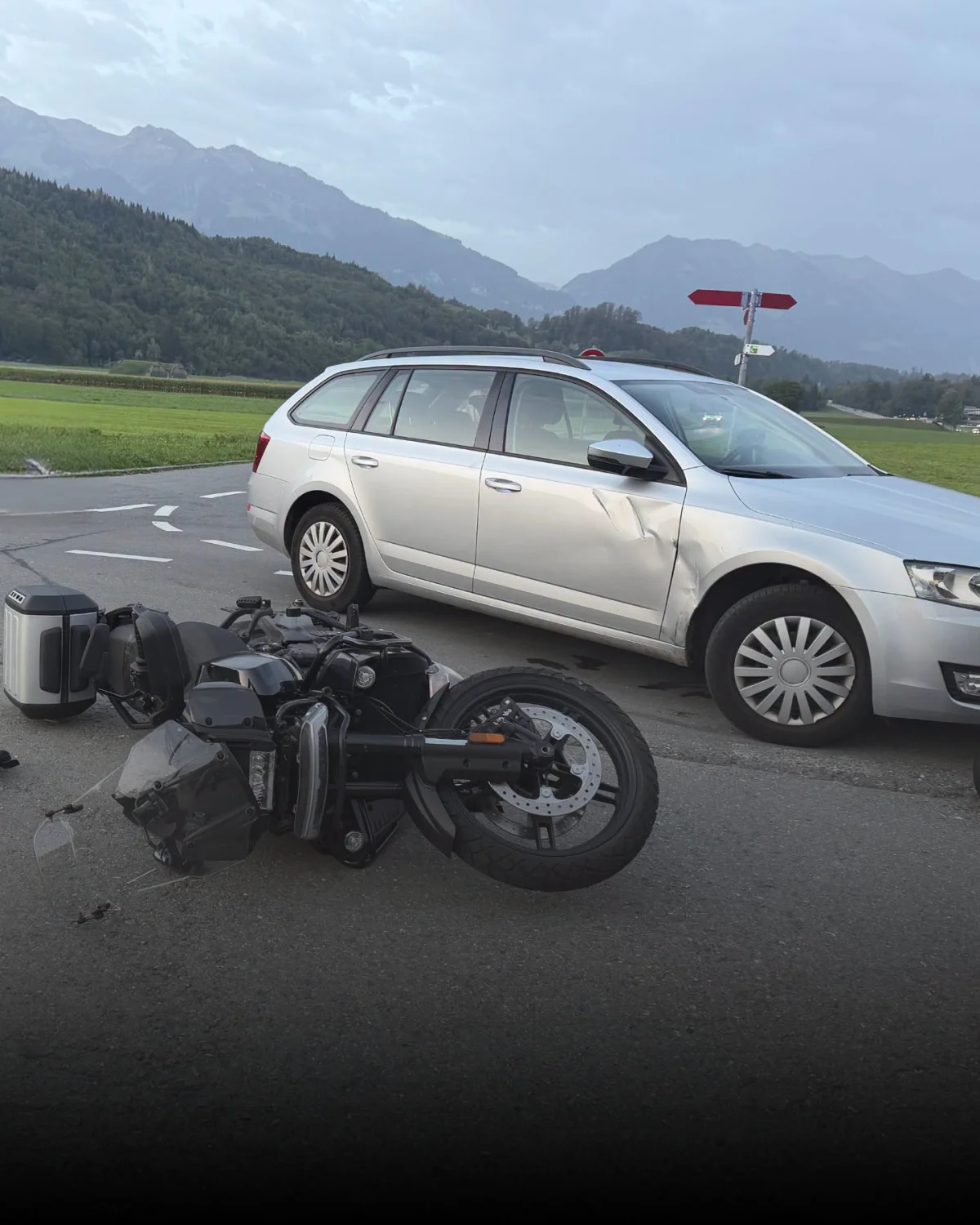 Auf einer Landstraße liegt ein umgefallenes Motorrad neben einem silbernen Auto mit sichtbarem Schaden an der Seite.