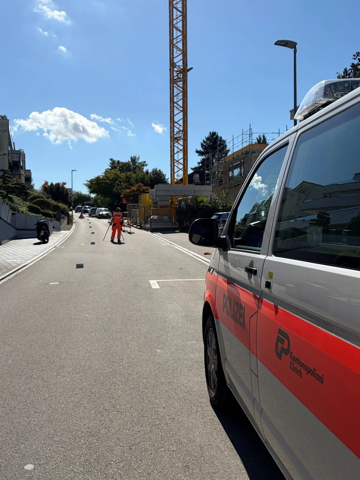 Auf dem Bild ist ein Polizeifahrzeug der Kantonspolizei Zürich zu sehen, das am Straßenrand parkt. Im Hintergrund sind Bauarbeiter und ein Kran zu sehen.