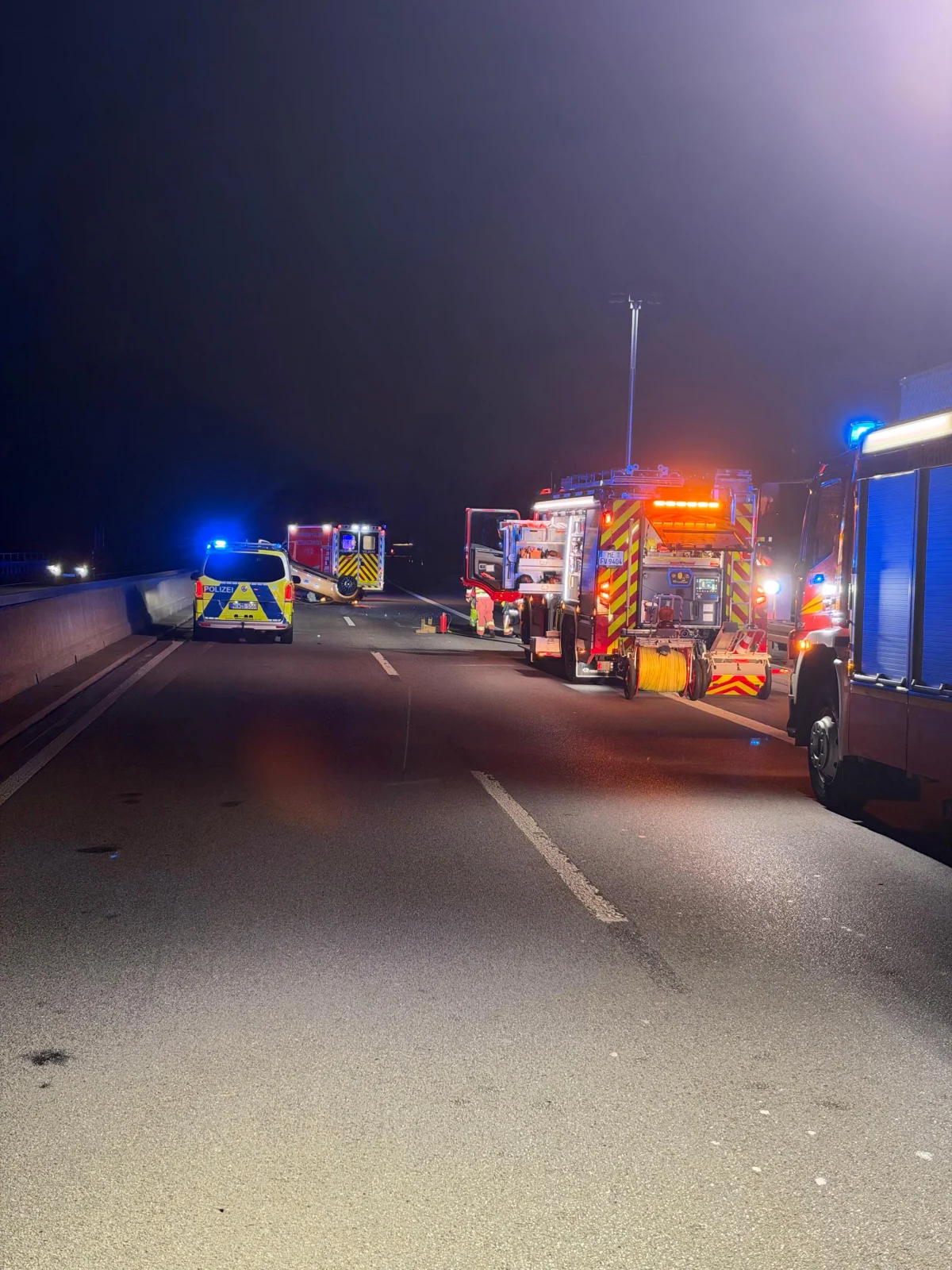 Mehrere Einsatzfahrzeuge mit Blaulicht stehen auf einer Autobahn bei Nacht. Feuerwehrfahrzeuge und ein Polizeifahrzeug sind zu sehen.