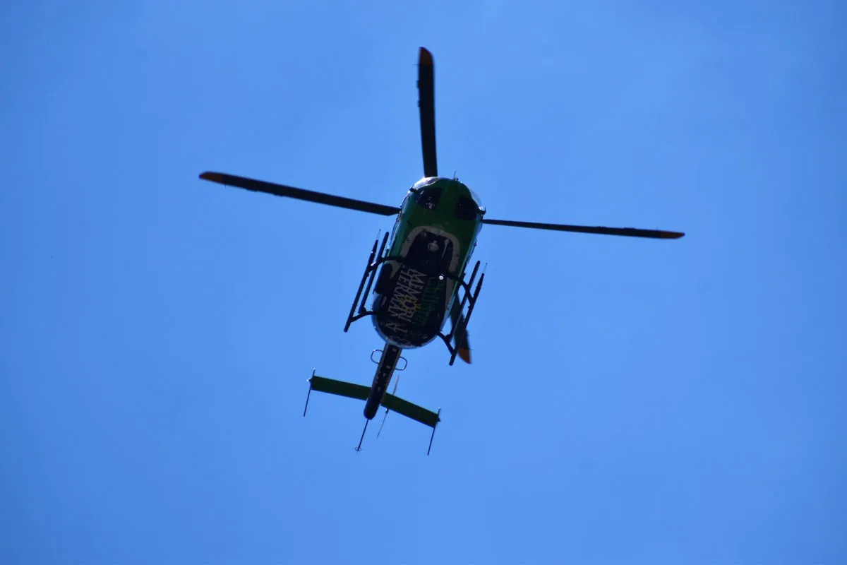 Ein grüner Helikopter ist von unten gegen den blauen Himmel zu sehen, fliegend mit ausgebreiteten Rotorblättern.