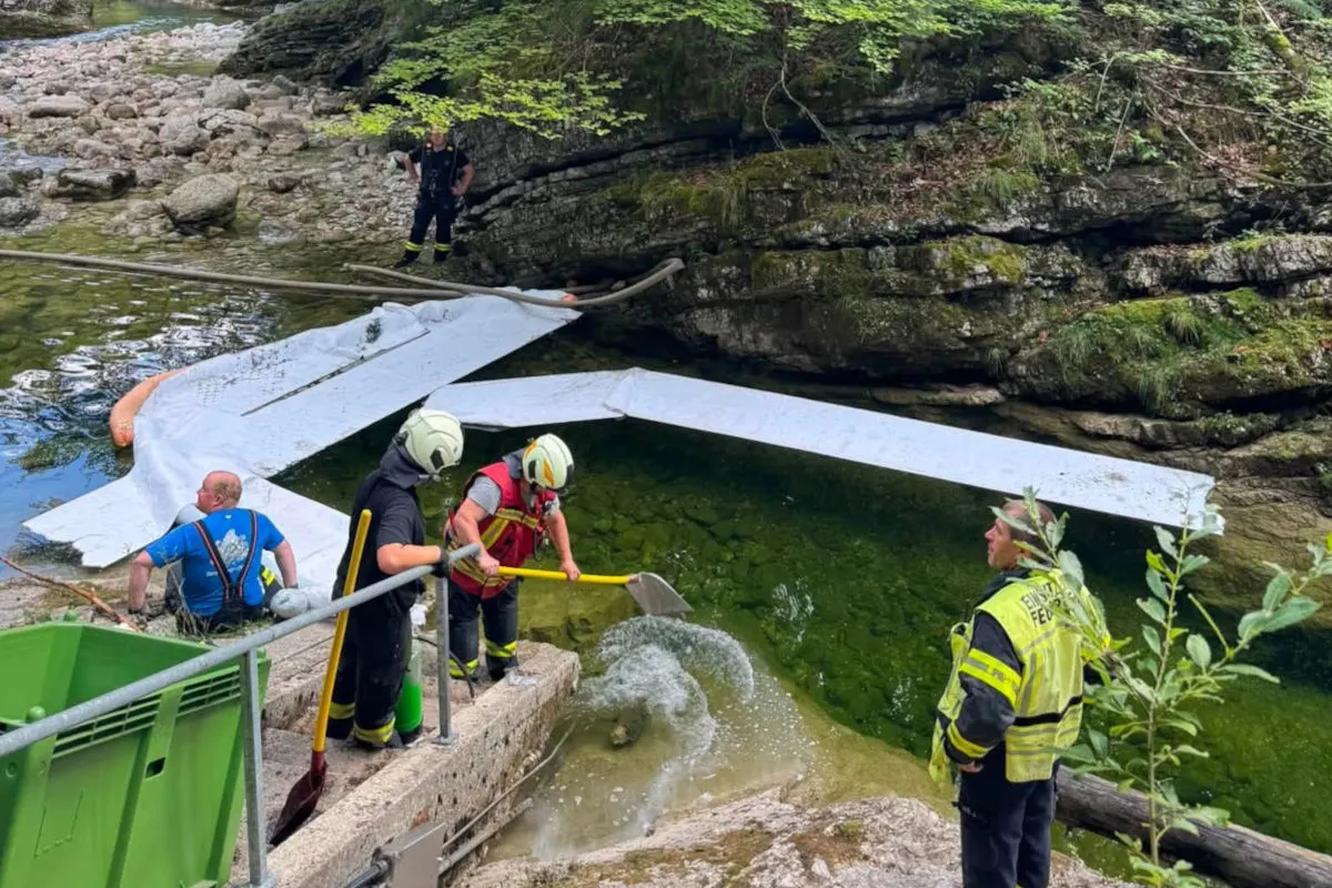 Mehrere Feuerwehrleute stehen an einem Fluss und platzieren eine schwimmende Sperre. Die Umgebung ist bewaldet und felsig.