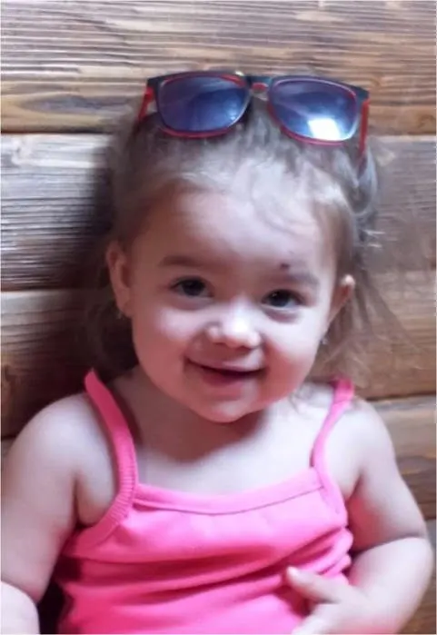 Ein kleines Mädchen mit rosa Trägerhemd lächelt in die Kamera. Sie trägt eine Sonnenbrille auf dem Kopf.