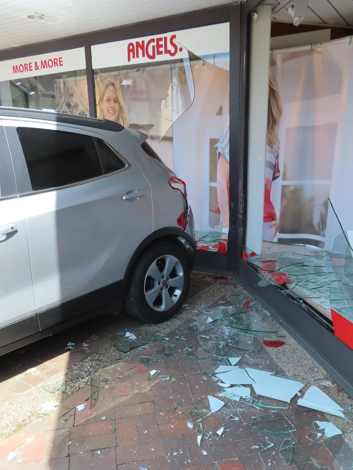 Ein silbernes Auto steht in einem Geschäftseingang, nachdem es die Glasfassade durchbrochen hat. Zahlreiche Scherben liegen auf dem Boden verstreut.
