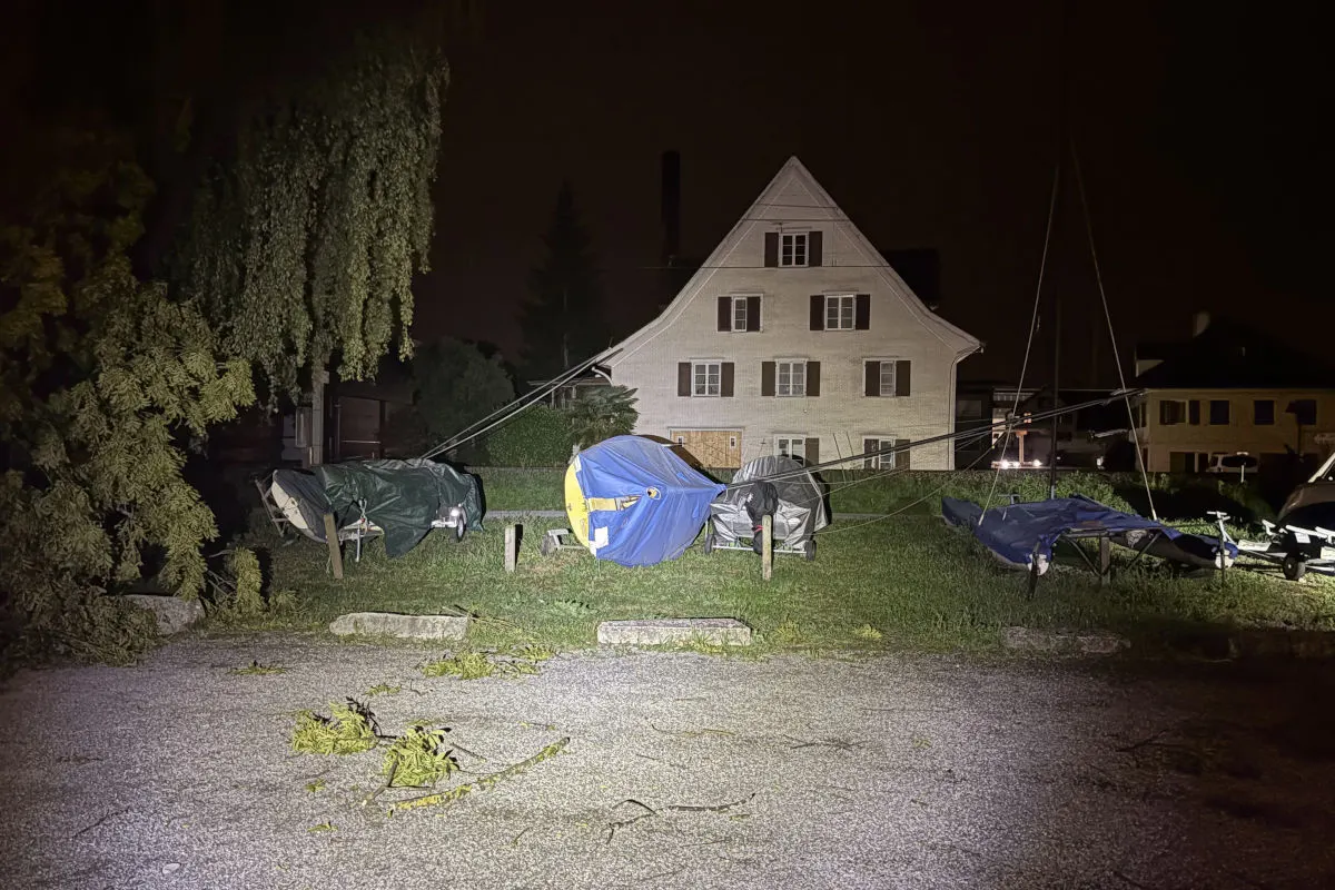 Mehrere Boote sind mit Planen abgedeckt und auf einem Grundstück abgestellt. Im Hintergrund befindet sich ein mehrstöckiges Haus. Das Bild wurde nachts aufgenommen.
