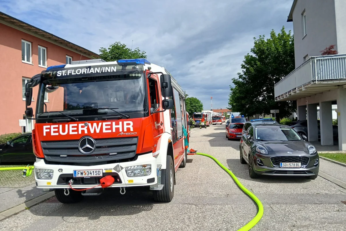 Ein Feuerwehrwagen mit der Aufschrift 'ST. FLORIAN/INN' steht auf einer Straße. Weitere Einsatzfahrzeuge und Autos sind sichtbar.