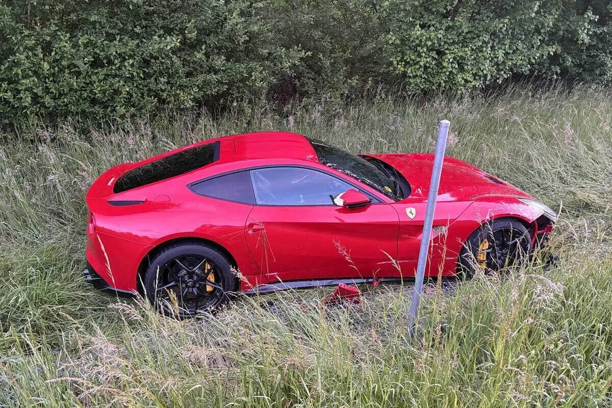 Ein rotes Auto ist von der Straße abgekommen und steht im hohen Gras neben einigen Bäumen. Es scheint keine Menschen in der Nähe zu geben.