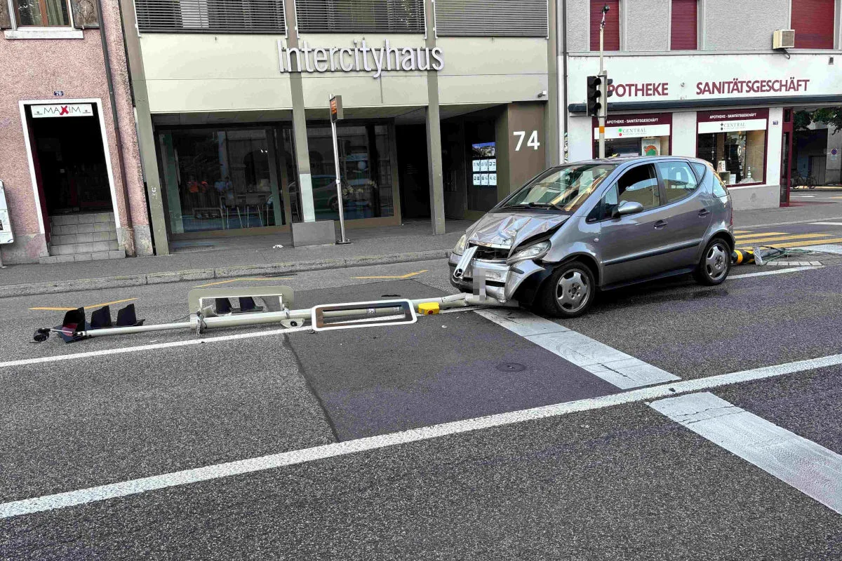 Das Bild zeigt ein beschädigtes Auto, das neben einem umgefallenen Verkehrsschild vor einem Gebäude auf einer Stadtstraße steht.