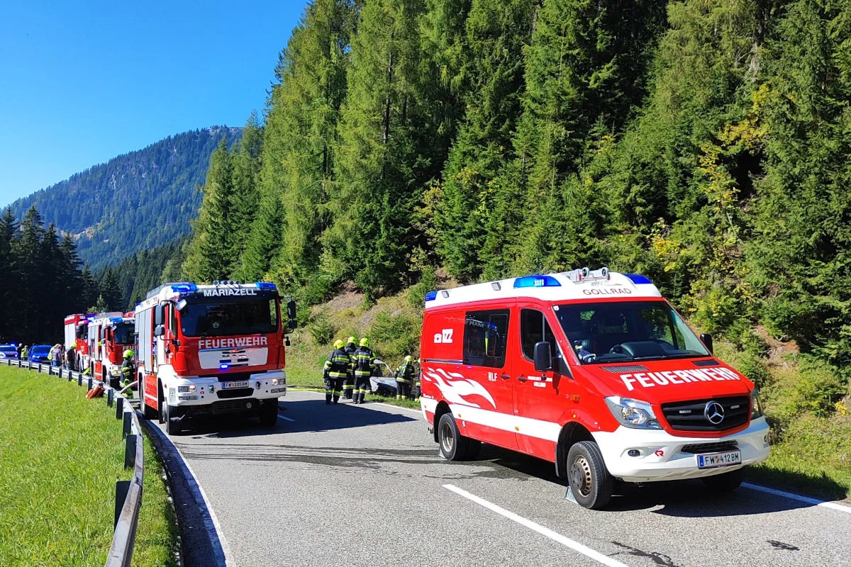 Mehrere Feuerwehrfahrzeuge und Feuerwehrleute sind auf einer Landstraße von Wäldern umgeben im Einsatz. Fahrzeuge aus Mariazell und Gollrad sind sichtbar.