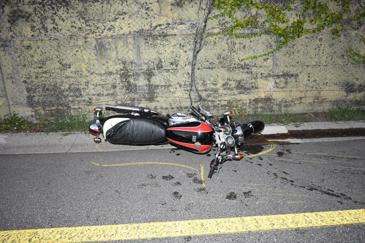 Ein umgestürztes Motorrad liegt auf der Seite auf der Straße. Im Hintergrund ist eine Mauer zu sehen.