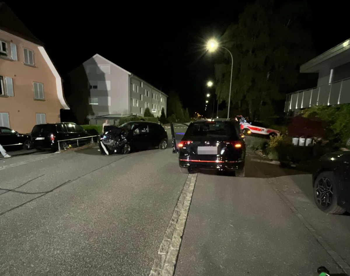 Ein Auto mit sichtbaren Schäden steht auf einer Wohnstraße bei Nacht. Im Hintergrund sind mehrere parkende Fahrzeuge zu sehen.