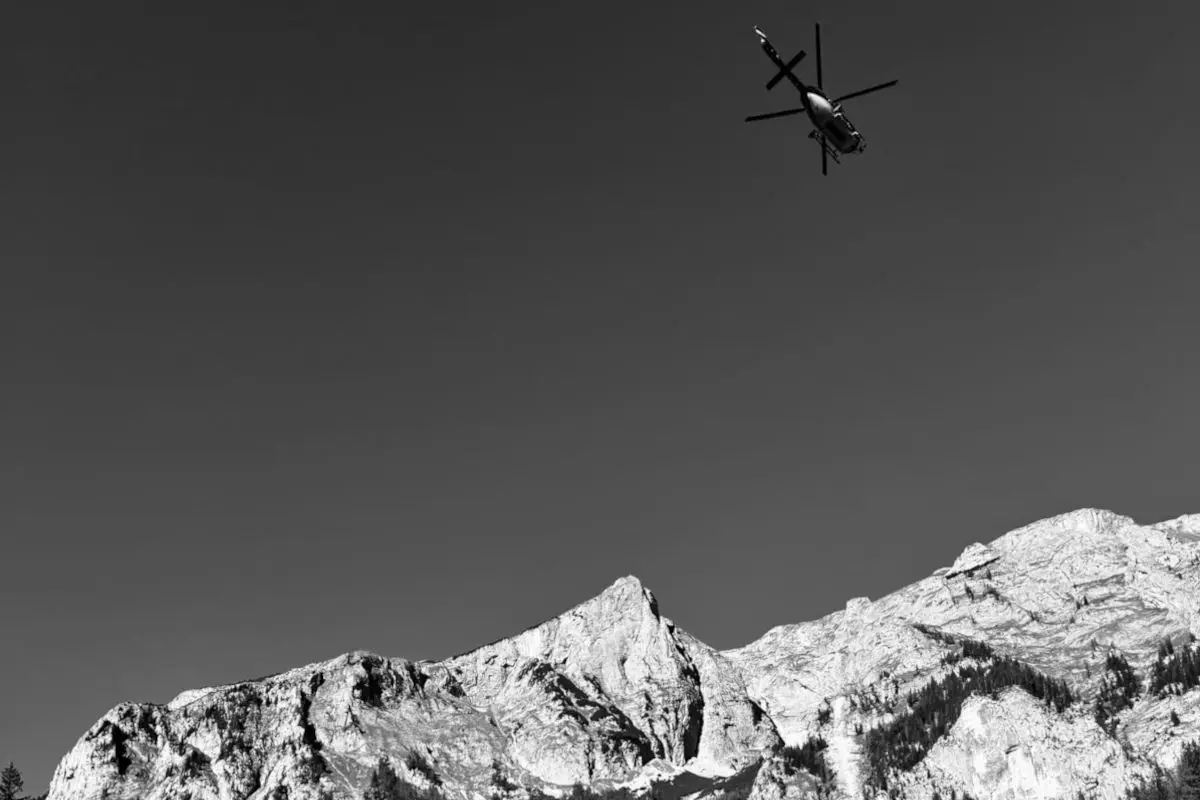 Ein einzelner Hubschrauber ist am Himmel zu sehen und fliegt über eine felsige Gebirgslandschaft unter klarem Himmel.