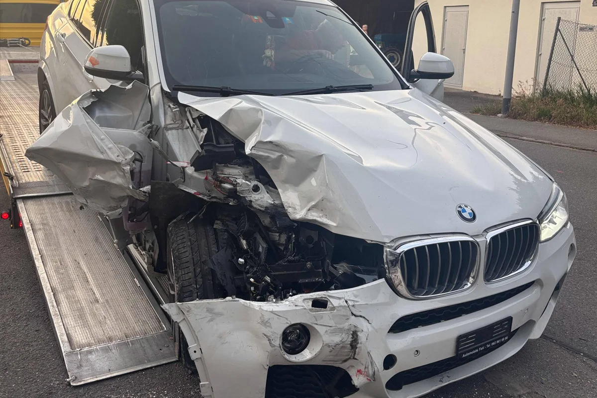 Ein weißer BMW X5 mit schwerem Frontschaden steht auf einem Abschleppwagen. Der linke vordere Bereich des Fahrzeugs ist stark verformt.