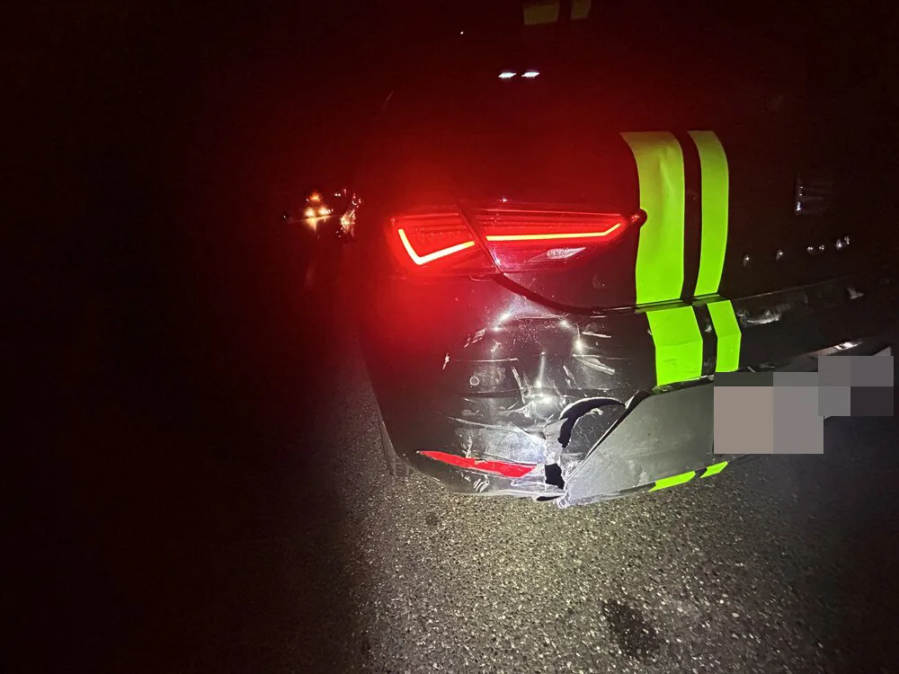 Das Bild zeigt ein Auto bei Nacht mit leuchtendem Rücklicht. Am Heck sind deutliche Schäden und Warnmarkierungen erkennbar.