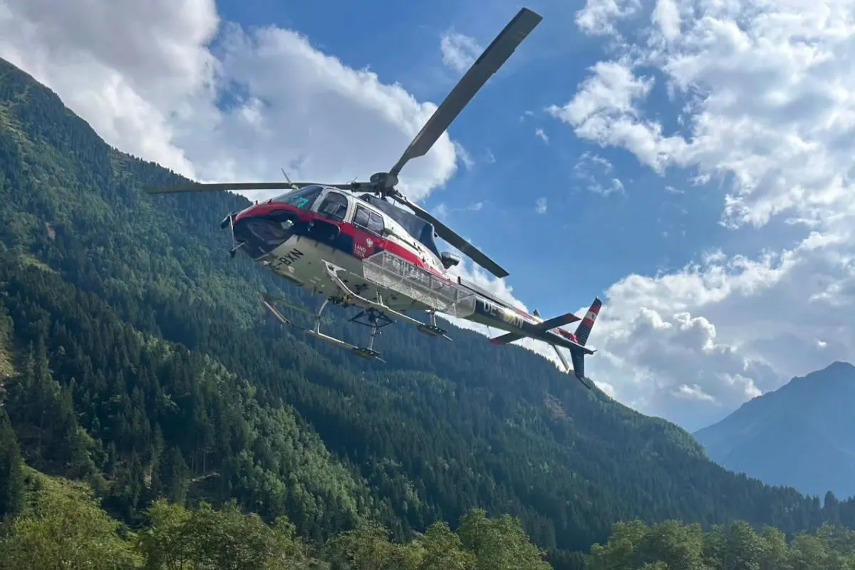 Ein Hubschrauber, gekennzeichnet mit Land Tirol, fliegt in einer alpinen Landschaft. Der Himmel ist teils bewölkt, aber klar.