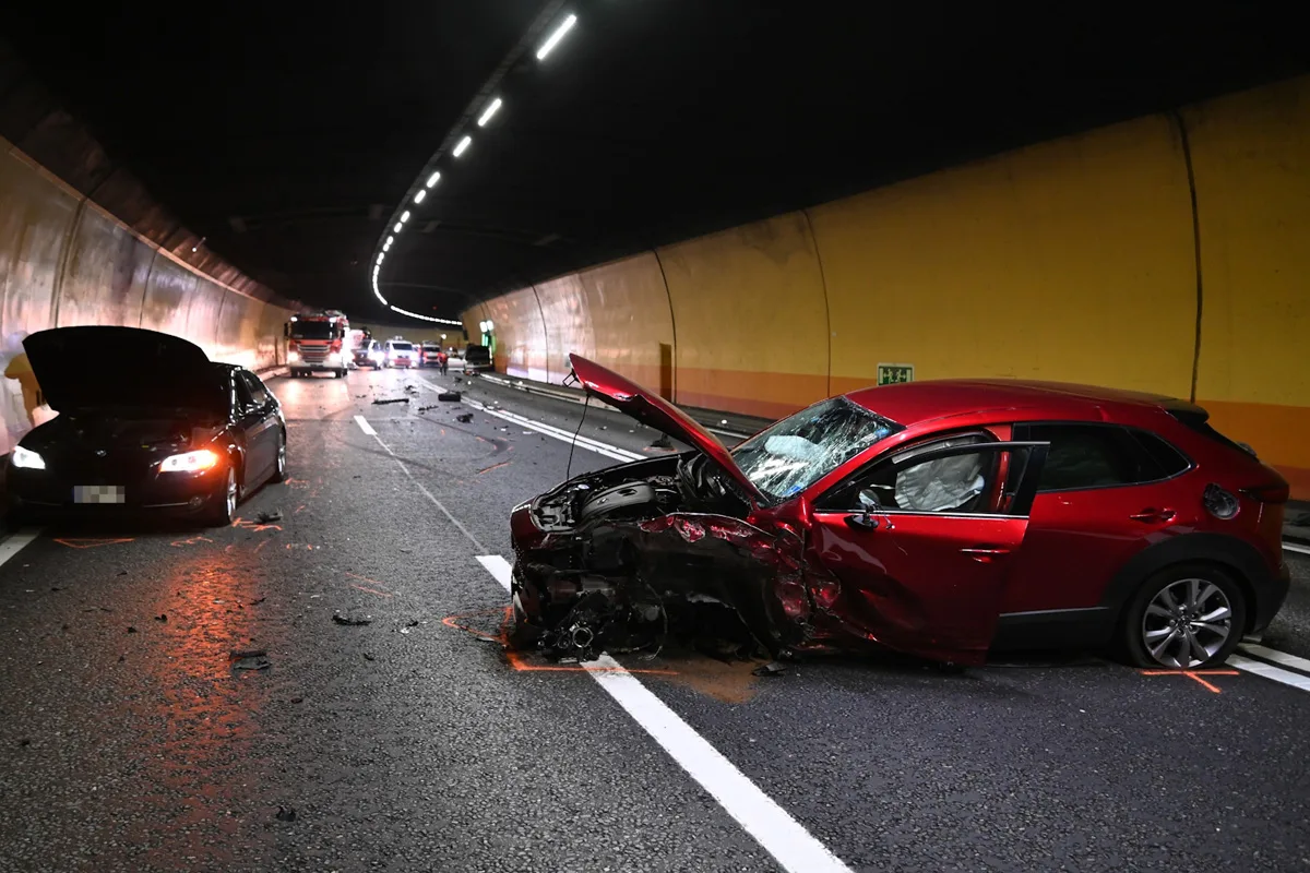 Im Tunnel stehen zwei stark beschädigte Fahrzeuge nach einem Unfall. Der Vorderteil eines roten Autos ist schwer deformiert.