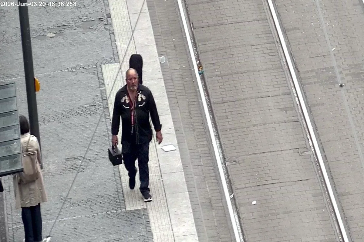 Ein Mann mit einer Tasche und einem Gitarrenkasten geht auf einem leeren Bahnsteig entlang.
