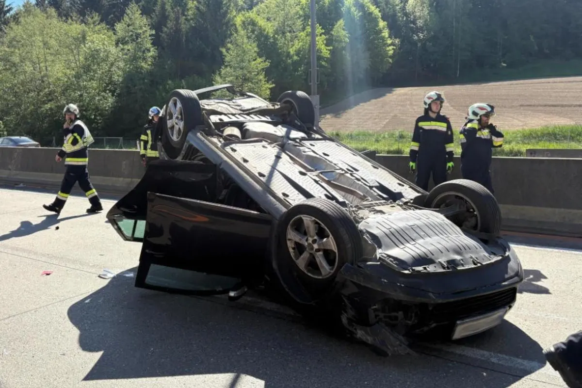 Ein Auto liegt auf dem Dach auf einer Straße. Im Hintergrund stehen Einsatzkräfte in Uniformen.