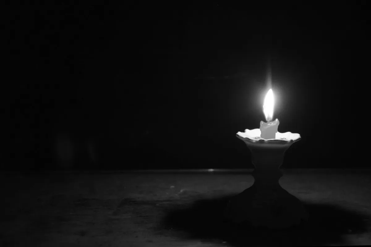 Das Bild zeigt eine einzelne brennende Kerze in einem dekorativen Kerzenhalter. Der Hintergrund ist dunkel und hebt das Licht der Flamme hervor.