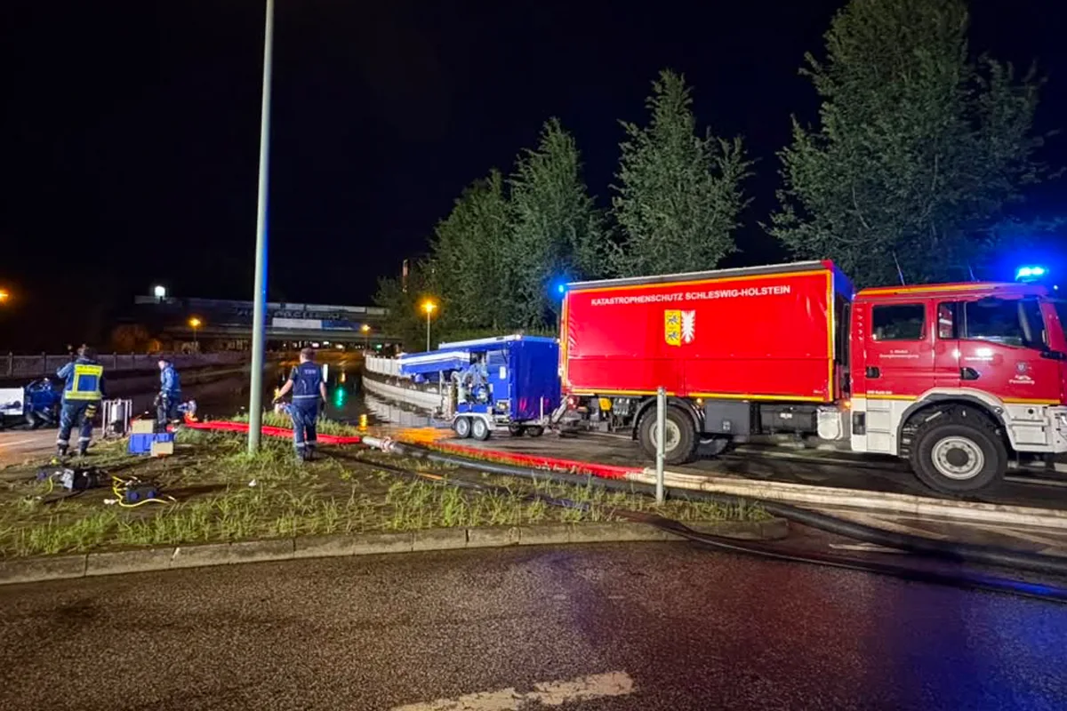 Zwei THW-Mitarbeiter arbeiten nachts am Flussufer mit einem großen roten Katastrophenschutzfahrzeug.