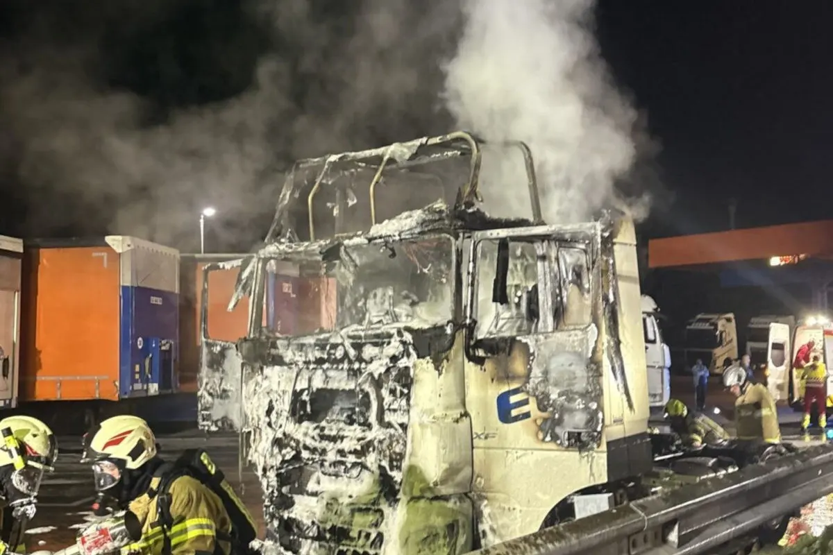 Ein schwer beschädigter, ausgebrannter LKW auf einer Straße bei Nacht. Feuerwehrleute arbeiten am Fahrzeug.
