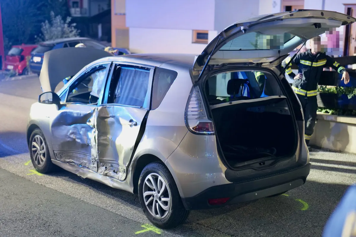 Ein Auto zeigt deutliche Schäden an der Seitentür. Der Kofferraum ist geöffnet, und eine Person in Uniform steht daneben.