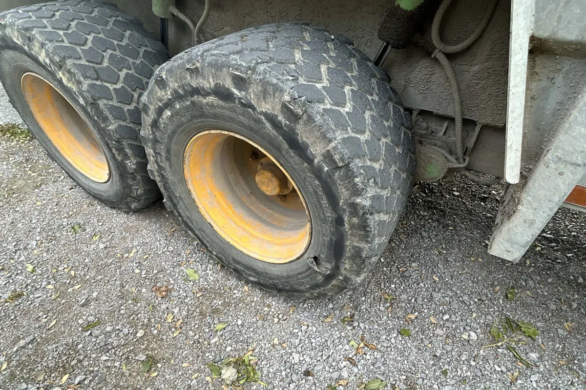 Ein großer Lkw-Reifen zeigt sichtbare Beschädigungen, während er auf einer Schotterstraße steht. Der Reifen wirkt abgenutzt und beschädigt.