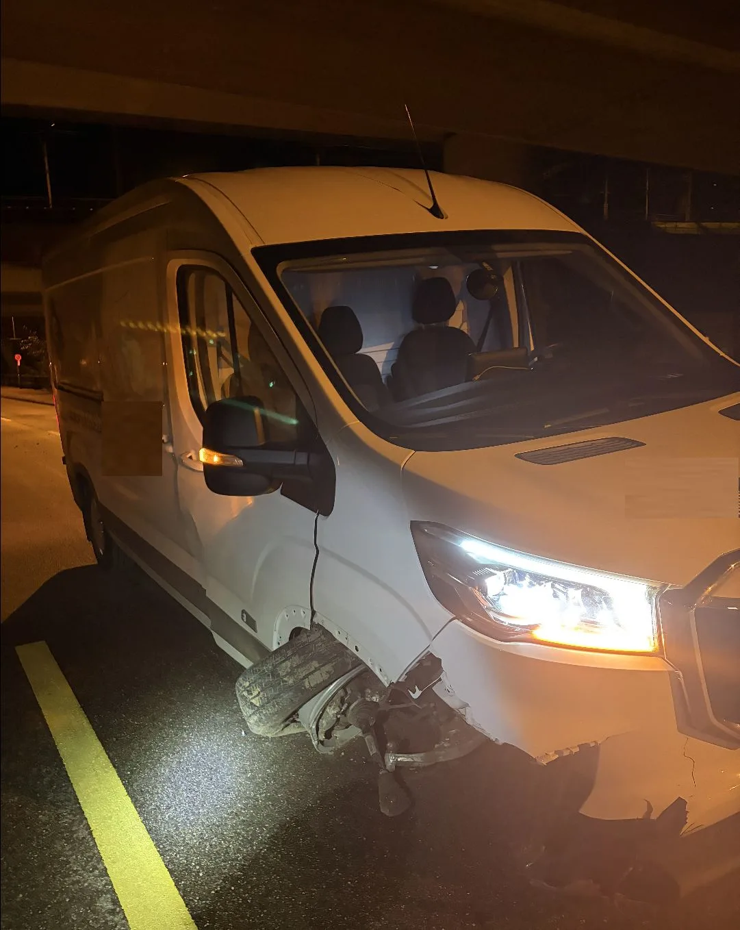 Ein weißer Lieferwagen steht mit einem abgerissenen Vorderrad auf einer Straße bei Nacht. Der Schaden ist an der rechten Vorderseite sichtbar.