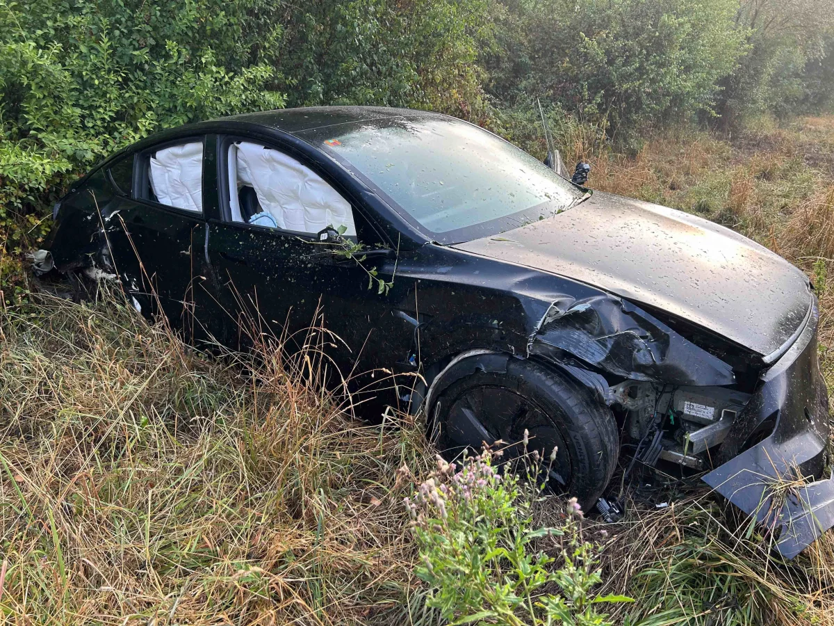 Ein schwarzes Auto mit erheblichen Frontschäden liegt schräg in einer bewachsenen Böschung. Die Airbags sind aktiviert.