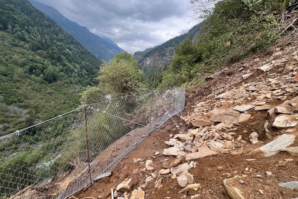 Ein steiler Hang in einer Berglandschaft mit einem Schutzzaun, der eine erdige und steinige Oberfläche sichert.