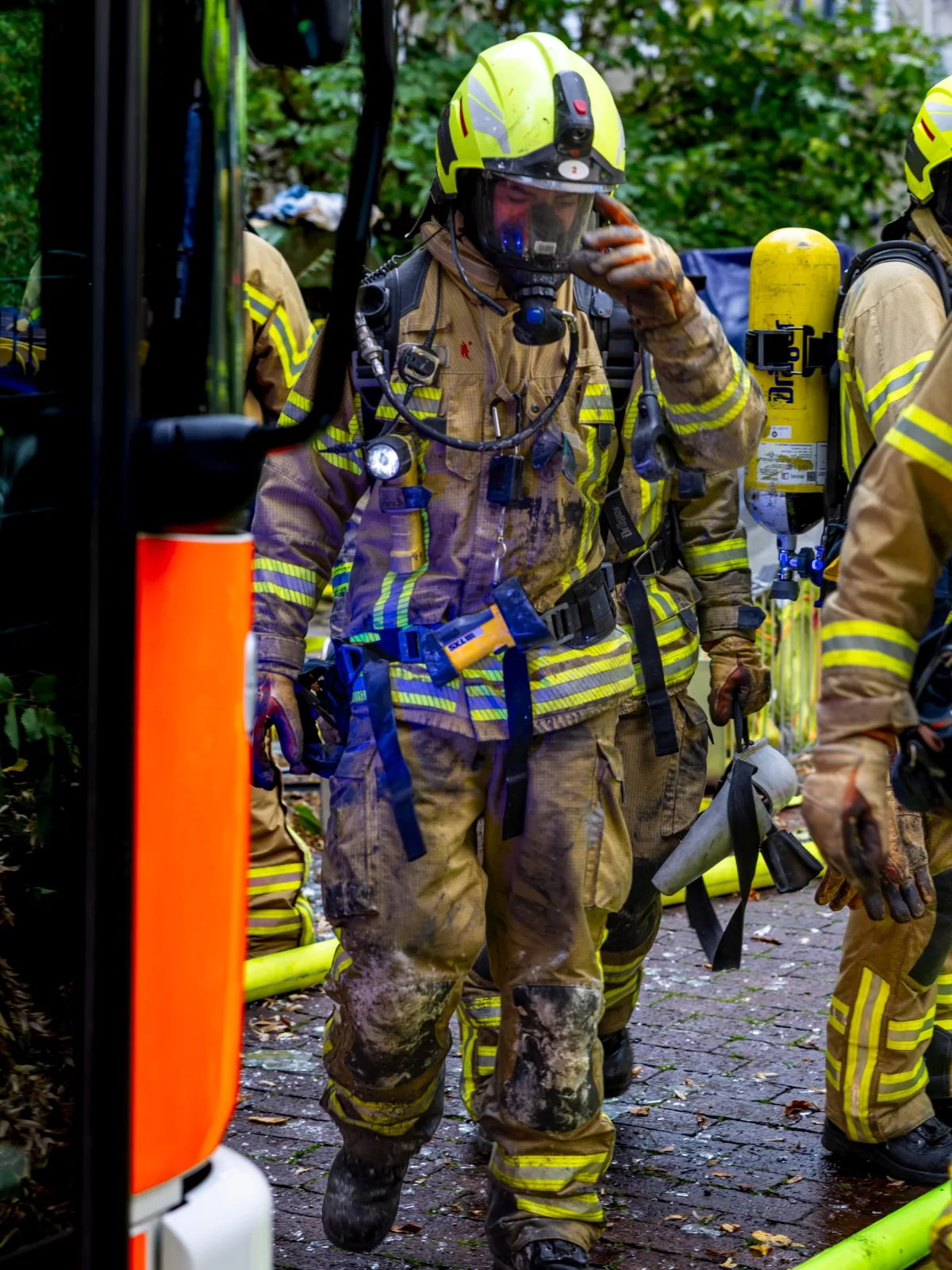 Mehrere Feuerwehrleute in schmutzigen Schutzanzügen tragen Atemmasken und Sauerstoffgeräte bei einem Einsatz im Freien.
