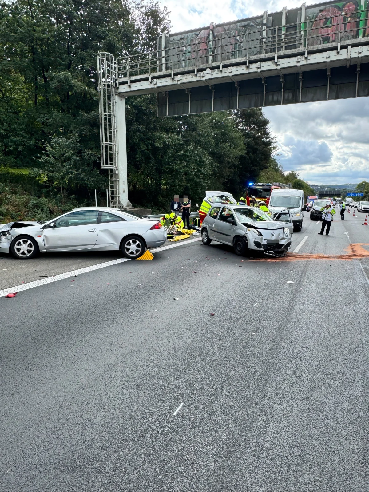 Mehrere beschädigte Autos stehen auf einer Autobahn unter einer Überführung, Rettungskräfte sind im Einsatz und sichern die Unfallstelle.