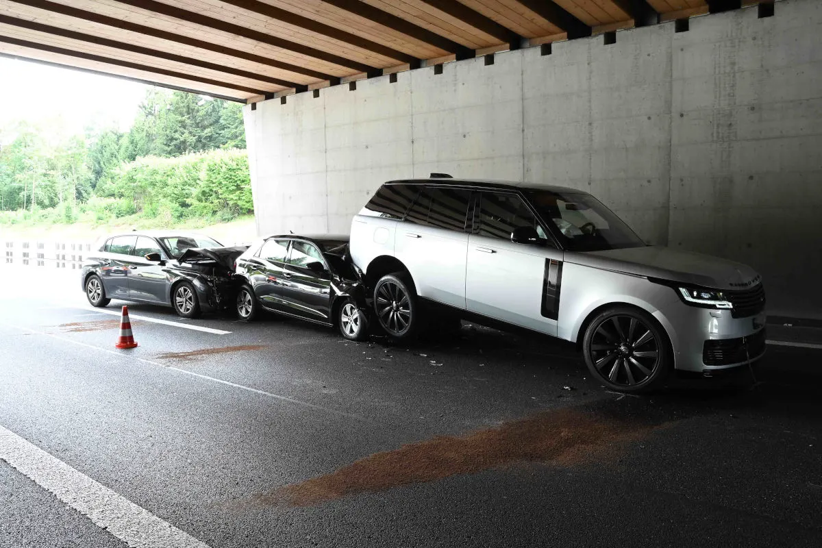 Drei Autos sind in einen Auffahrunfall unter einer Brücke verwickelt. Die Fahrzeuge sind beschädigt, und es steht ein Verkehrskegel in der Nähe.