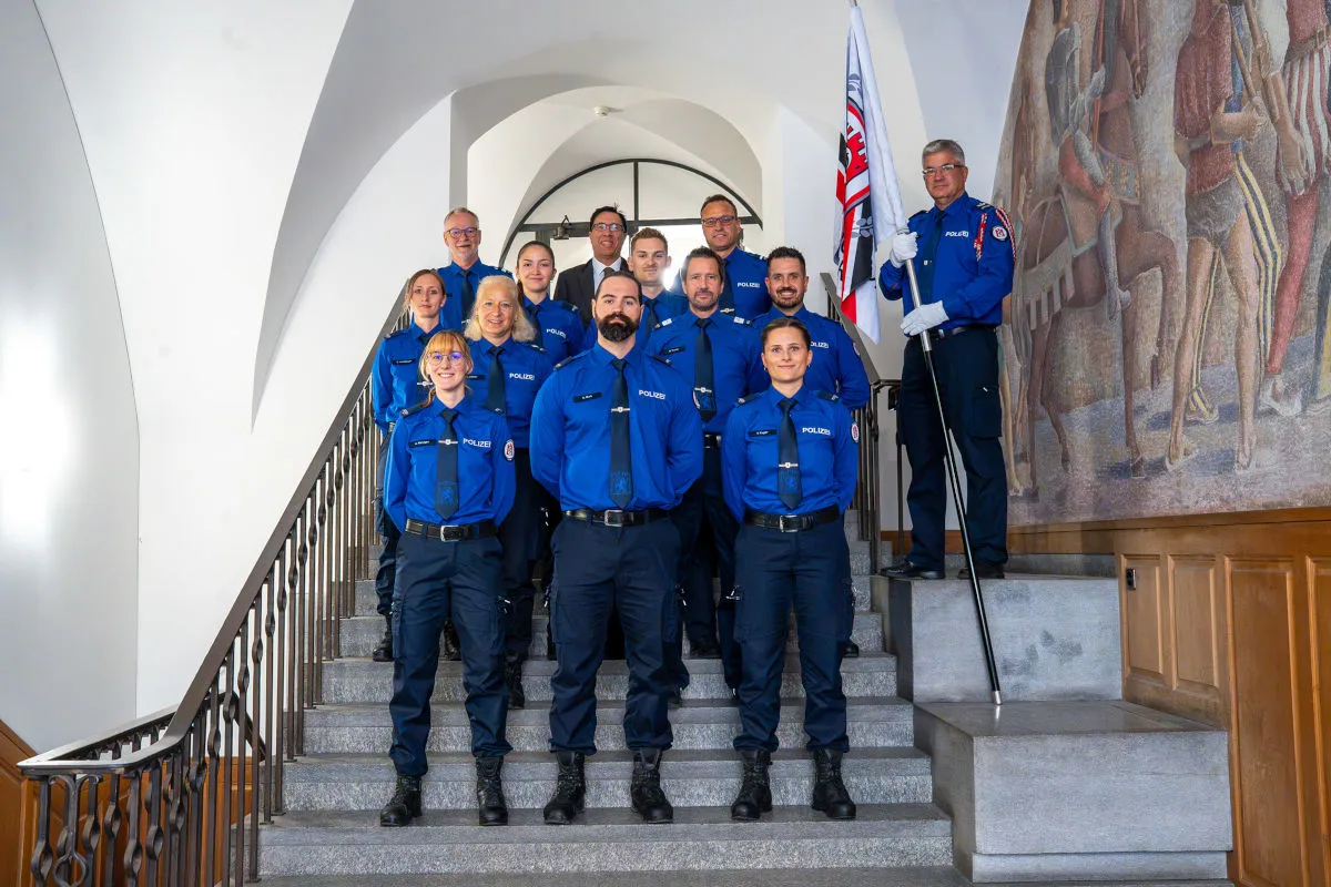 Eine Gruppe von Polizeibeamten in blauen Uniformen steht geordnet auf einer Treppe. Einer von ihnen hält eine Fahne.