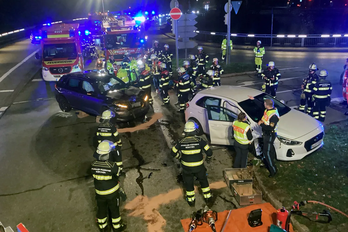 Zwei Autos sind auf einer Kreuzung kollidiert. Feuerwehrleute in Schutzkleidung sind anwesend und sichern die Unfallstelle.