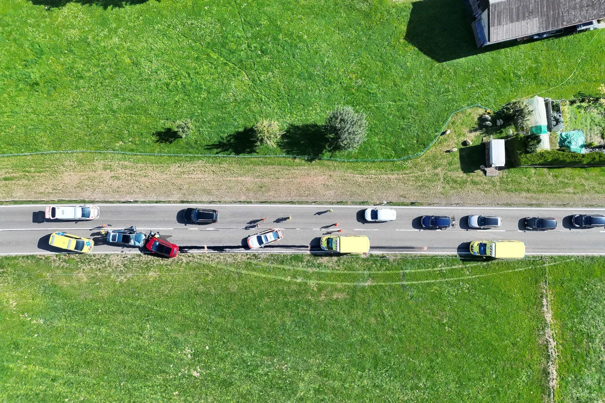 Eine Drohnenaufnahme zeigt eine Landstraße mit mehreren kollidierten Autos und Einsatzfahrzeugen. Einsatzkräfte sind vor Ort.