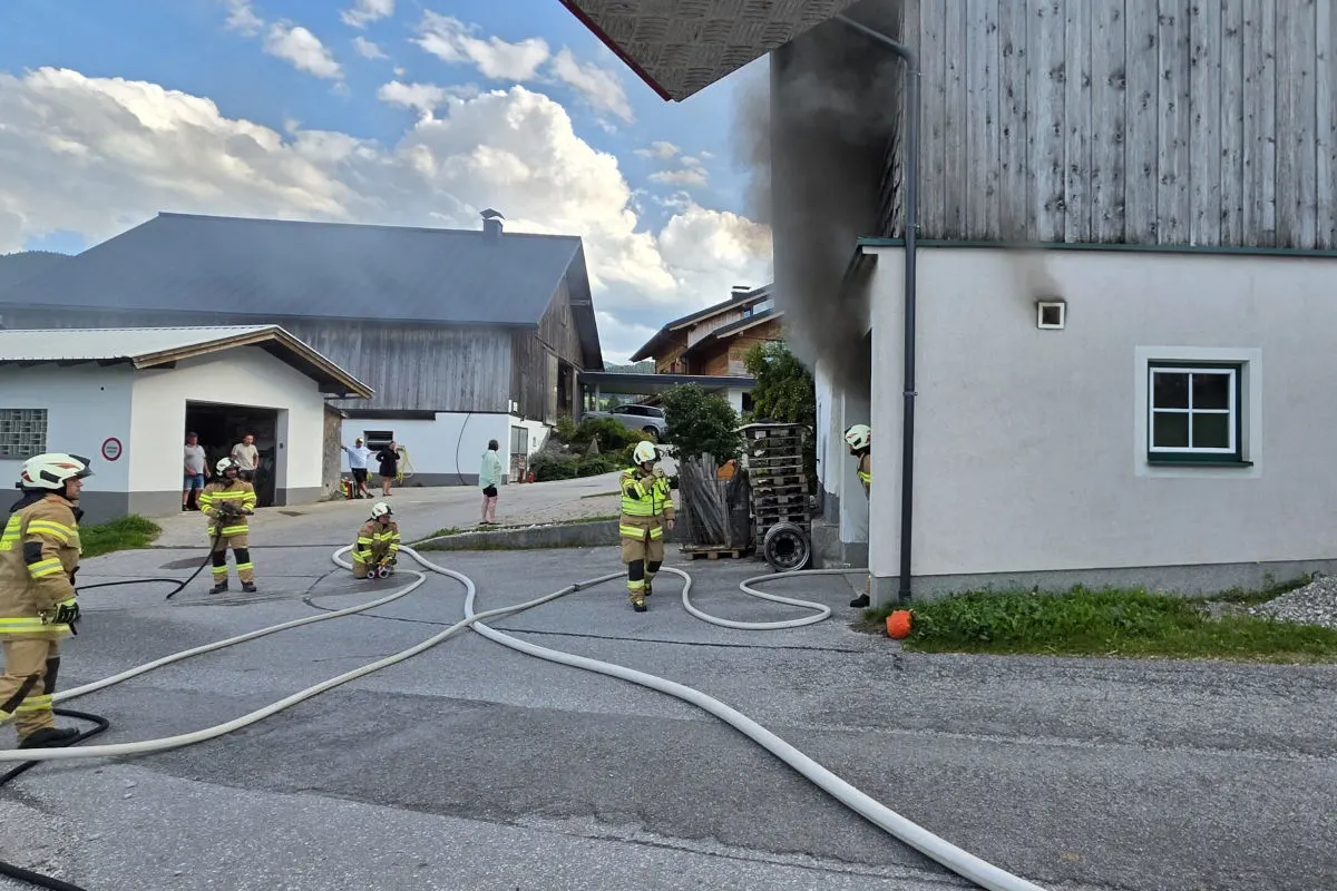 Mehrere Feuerwehrleute stehen vor einem Gebäude, aus dem schwarzer Rauch aufsteigt. Feuerwehrschläuche sind ausgelegt.