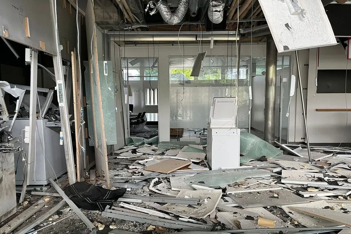 Ein schwer beschädigtes Büro ist mit Schutt und heruntergefallenen Deckenteilen übersät. Kabel hängen von der Decke herab, und zerbrochene Möbel sind zu sehen.