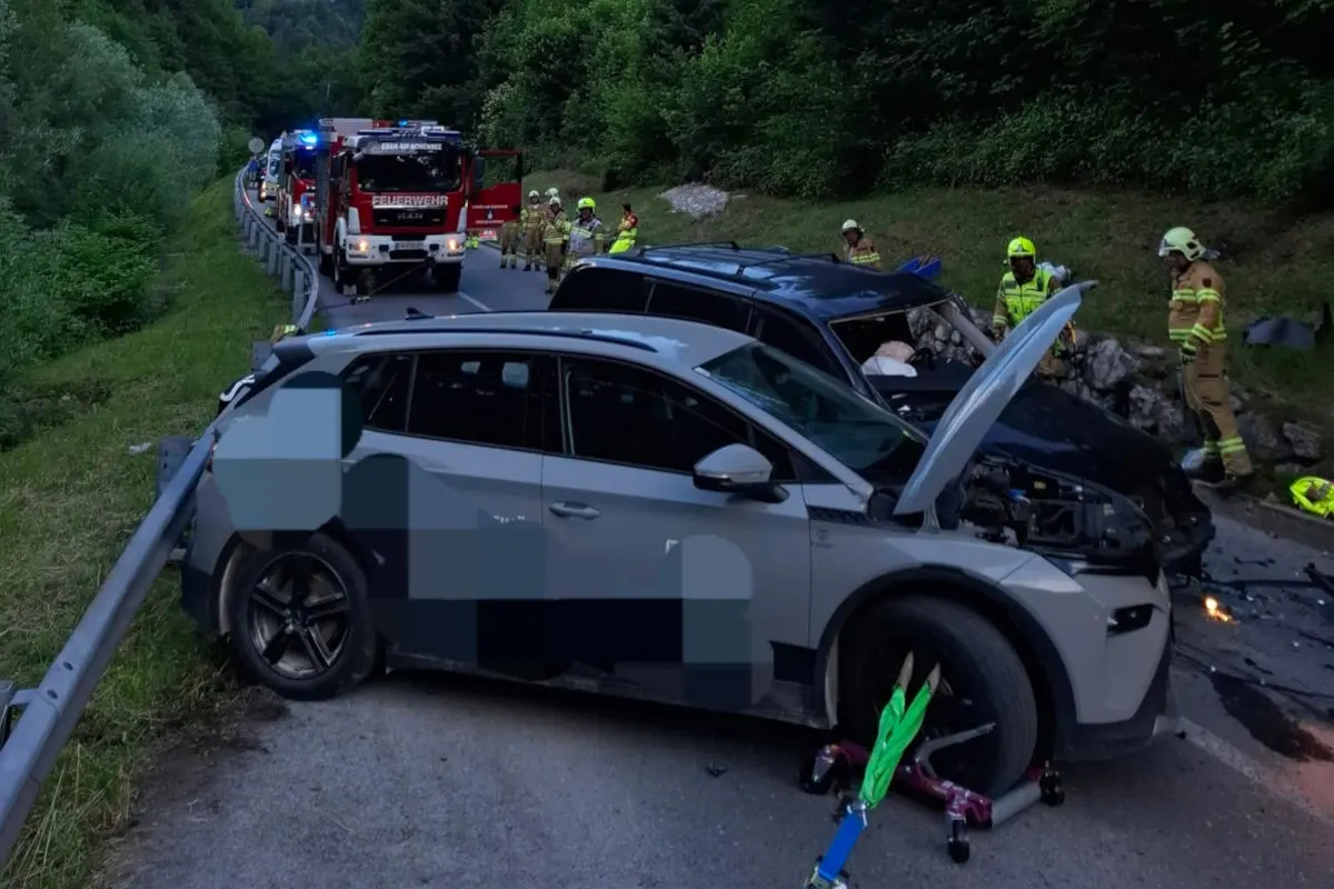 Zwei beschädigte Autos stehen auf einer Landstraße, während Feuerwehrleute die Unfallstelle absichern. Im Hintergrund sind Einsatzfahrzeuge zu sehen.