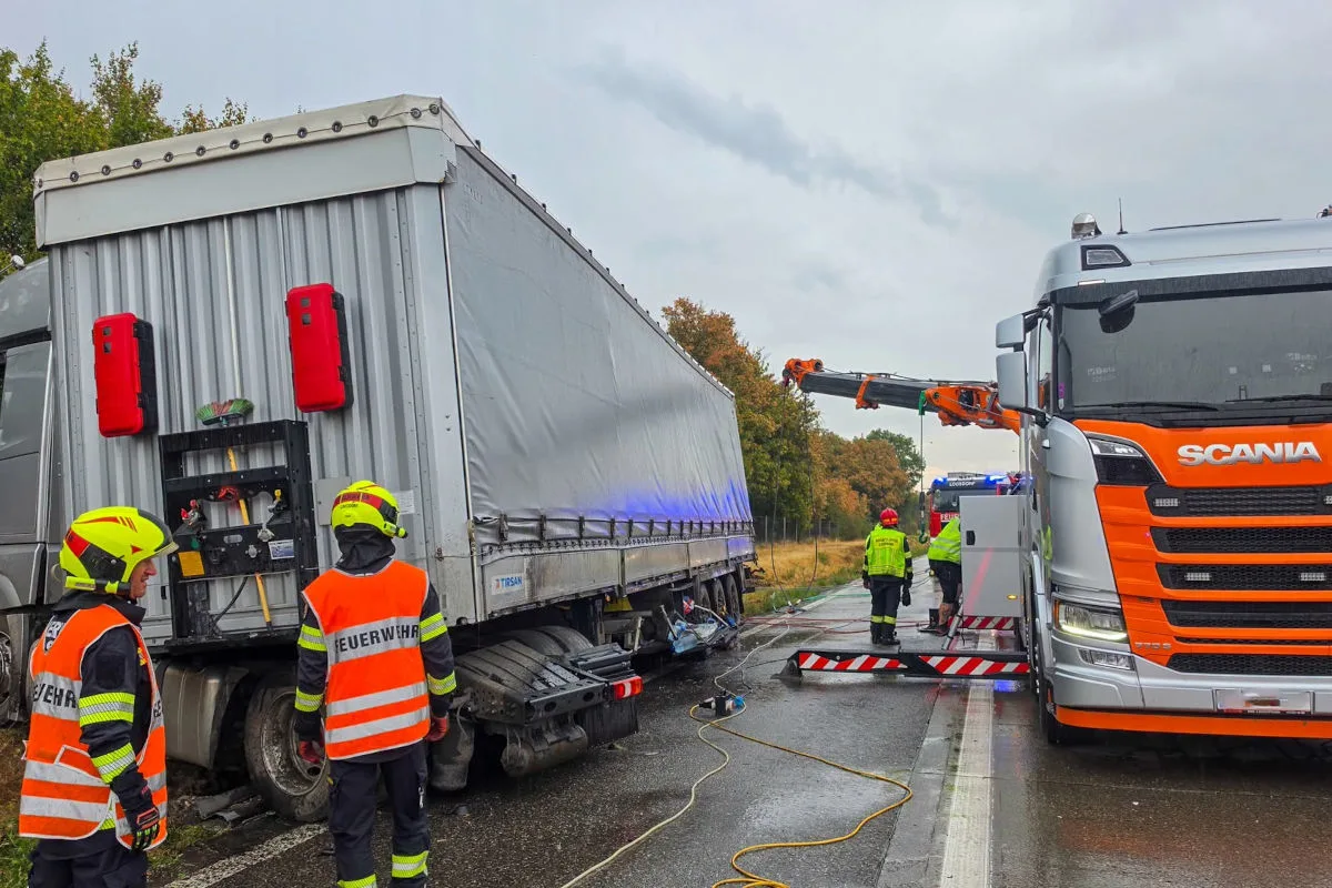 Mehrere Feuerwehrleute sind an einem verunfallten Lastwagen auf einer regennassen Straße im Einsatz. Ein Kranfahrzeug der Feuerwehr ist ebenfalls vor Ort.