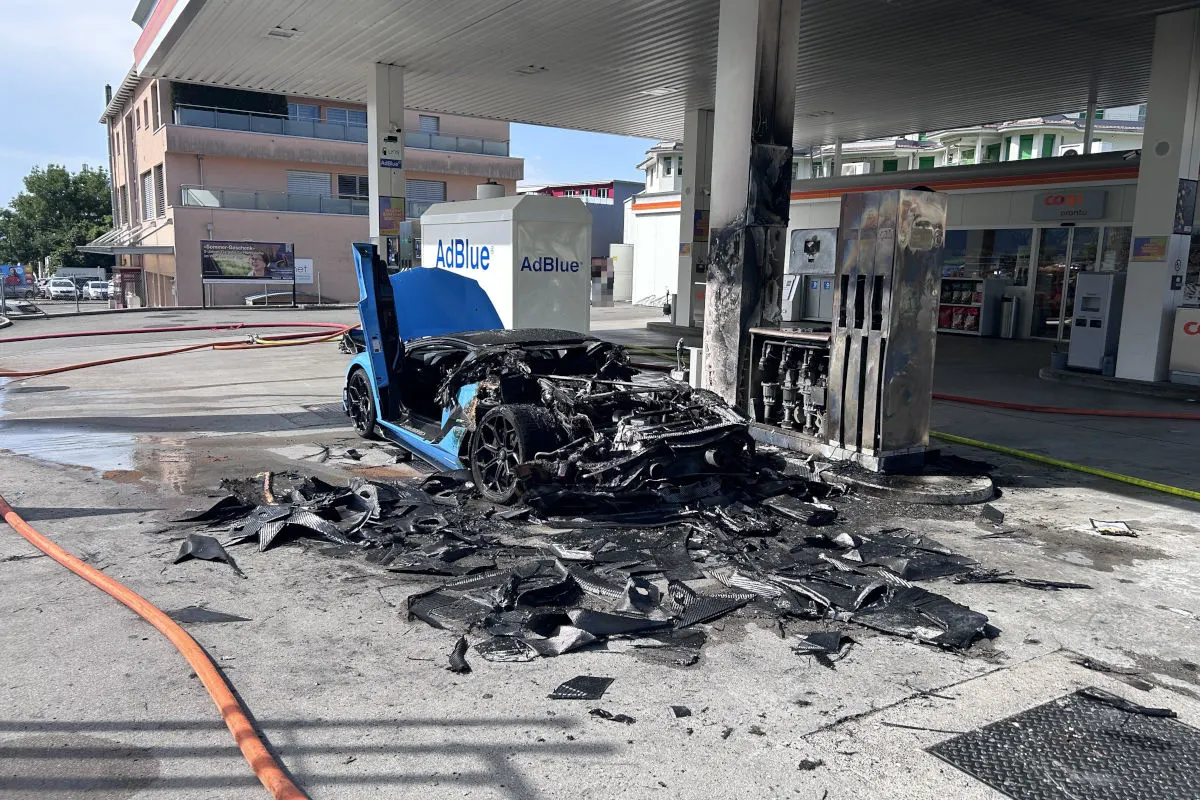 Ein völlig ausgebranntes Auto steht vor einer Tankstelle, umgeben von verkohlten Trümmern und Rußspuren an einer Zapfsäule.