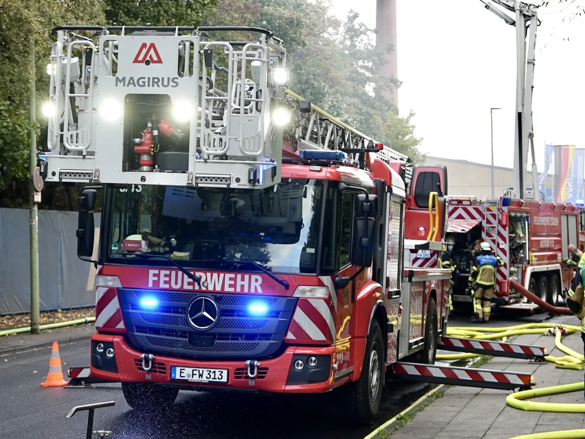 Ein rotes Feuerwehrfahrzeug mit ausgefahrener Leiter steht auf einer Straße. Feuerwehrleute sind im Einsatz neben weiteren Einsatzfahrzeugen.