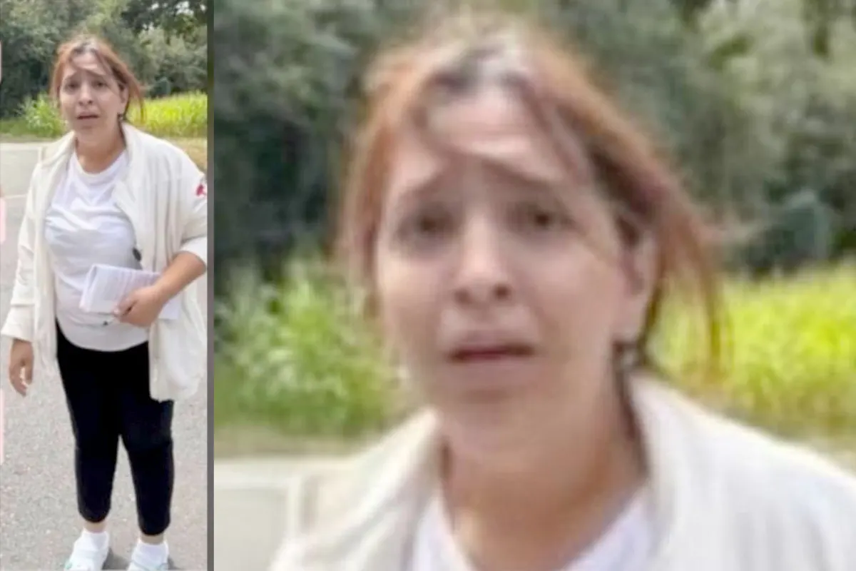Eine Frau mit weißen Shirt und Jacke hält Papiere, steht auf einer Straße im Freien und schaut in die Kamera.