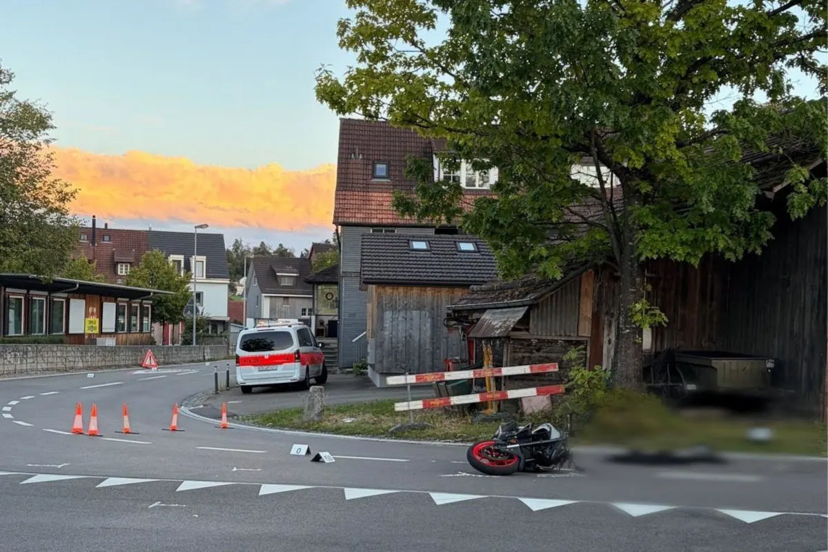 Ein gestürztes Motorrad liegt auf der Straße, im Hintergrund ist ein Polizei-Kleinbus sichtbar. Straßensperrungen durch Kegel und Warnschilder sind aufgestellt.